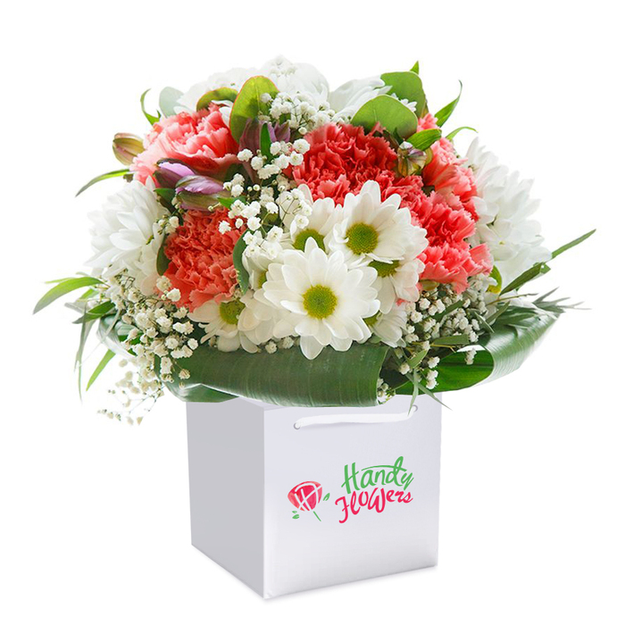 Perfect for expressing meaningful gestures throughout Leamouth, this thoughtfully arranged bouquet speaks of care and expert craftsmanship. Presented upright in a crisp, pristine white square gift bag, the ensemble features a sumptuous collection of coral-pink and deep red carnations-each blossom soft and frilled, creating a cascade of colour that draws the eye. Sprightly white daisies, each with a luminous lime-green center, recall the fresh blooms one might find blooming along the pedestrian paths of Bow Creek Ecology Park, lending a mood of natural joy. Gentle tufts of white baby's breath scatter through the bouquet, softening transitions and enhancing the overall sense of airy abundance. Along one edge, slightly closed buds in shades of purple and pink add an extra dimension, hinting at continuing growth and the unique seasonal rhythms of Leamouth gardens. All these elements are wrapped in a verdant collar of broad, glossy leaves, adding visual unity and a solid base to the rounded shape. Sturdy white ribbon handles make the gift bag as practical as it is elegant, ideal for effortless delivery to homes or offices in Leamouth. Set against an immaculate white backdrop, every hue and petal is vividly defined, communicating freshness and thoughtful curation-an arrangement just right for celebrating anniversaries, welcoming loved ones, or marking new chapters within Leamouth's riverside locale.