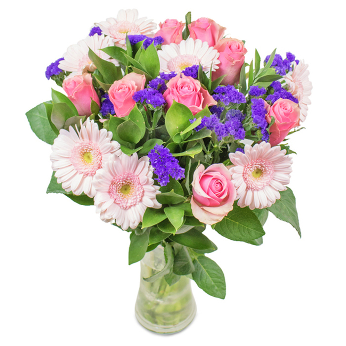 Poised elegantly in a clear glass vase against a neutral background, this eye-catching arrangement captures the fresh energy of Leamouth. The bouquet's center features approximately eight medium pink roses, some petals tipped with deeper hues, each spiraled and either tightly wrapped or unfolding, conjuring a sense of anticipation and classic beauty. About six opalescent gerbera daisies with large, round faces and delicately ruffled petals frame these roses, the centers so light they nearly blend into the brightness of a riverside morning. Interspersed are vibrant clusters of purple statice, their textured blooms and saturated colour creating a lively counterpoint, much like flashes of creativity amid the old warehouses of Orchard Place. Deep green leaves form a robust base and elegant frame, refreshing in both tone and scent, anchoring the blooms in natural abundance. The transparent vase showcases intertwined stems and clear water, hinting at the bouquet's freshness and the meticulous care of its Leamouth maker. Designed for special moments-be it a birthday surprise, Mother's Day celebration, or simply to grace a contemporary flat near Trinity Buoy Wharf-this bouquet radiates joyful intention and thoughtful composition, delivered with the warmth and pride of local craft.